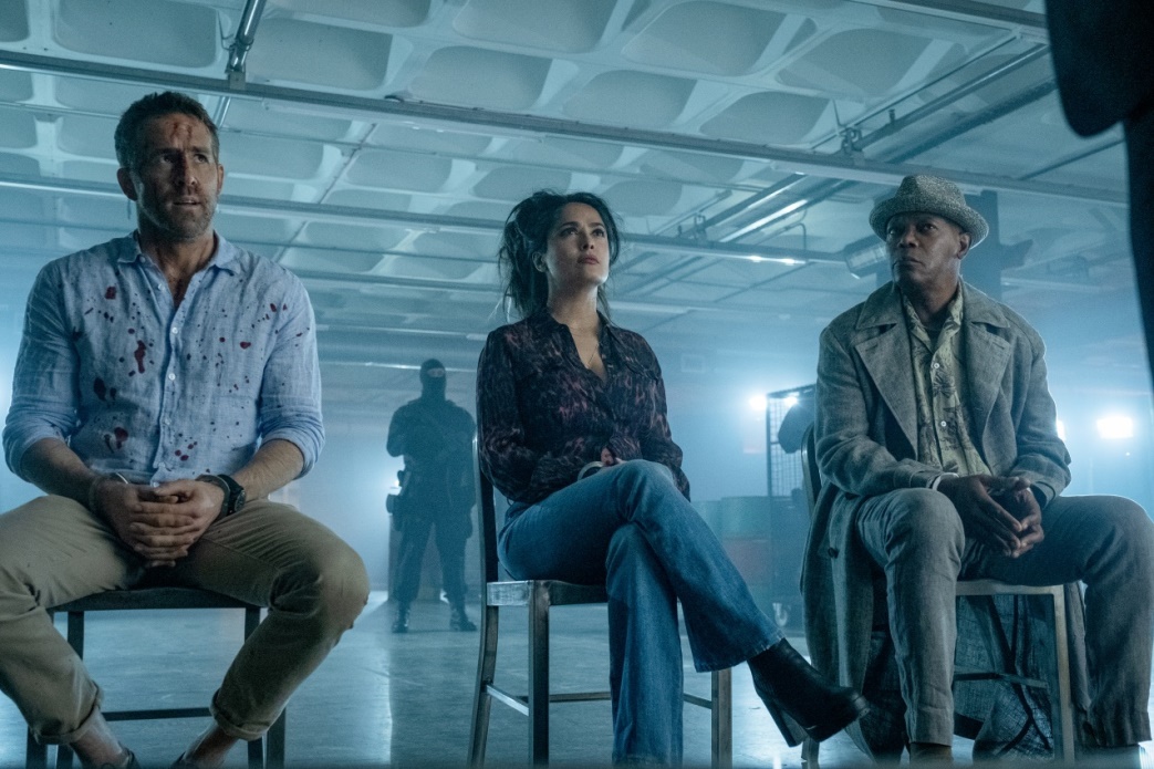 Ryan Reynolds, Selma Hayek und Samuel L.Jackson sitzend auf Stühlen nebeneinander, im Film Killers Bodyguard 2.