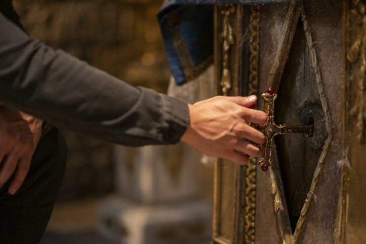 Eine Hand mit einem Kruzifix, dass als Schlüssel eine Tür öffnet im Film Uncharted