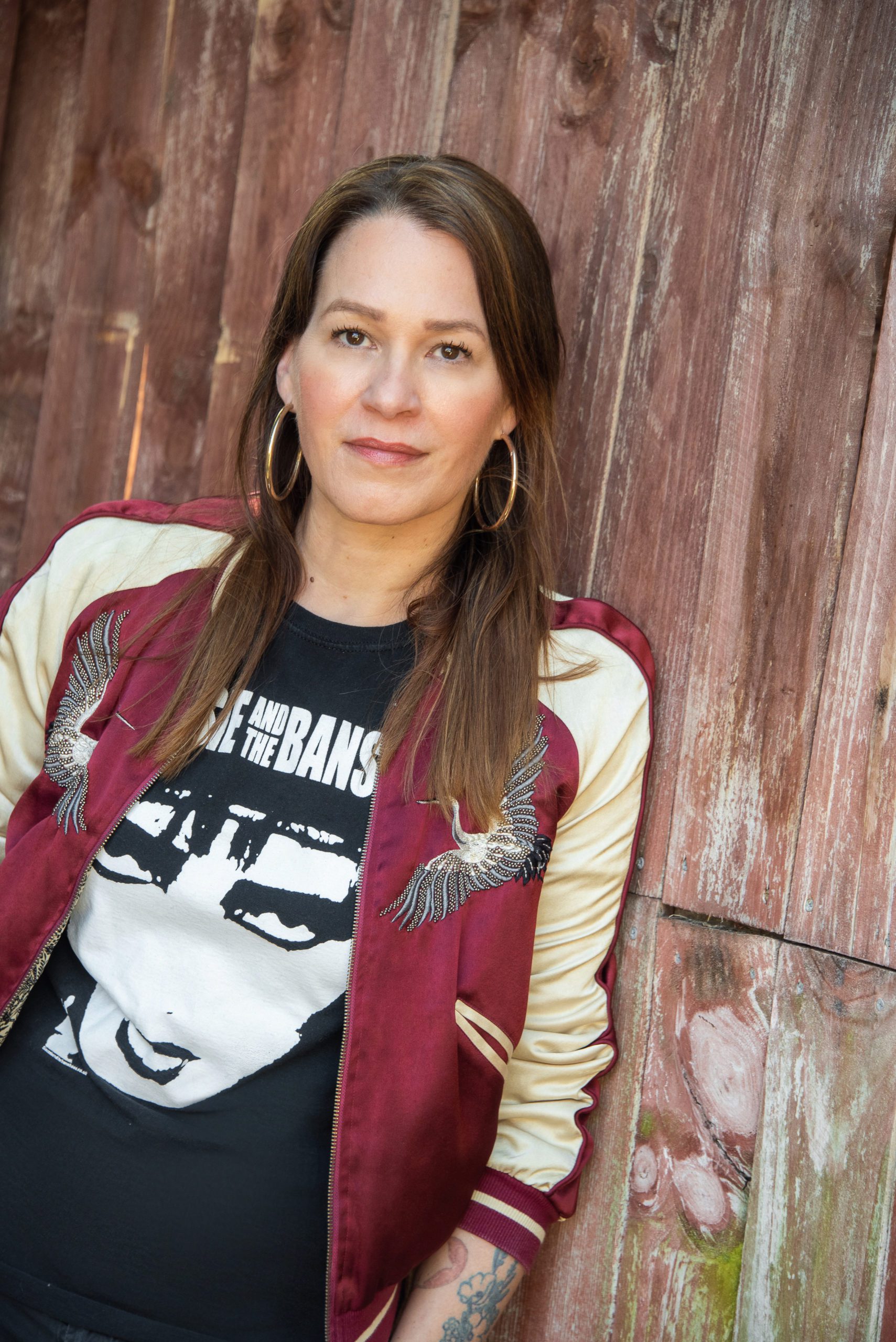 Franka Potente im roten, modischen Blouson lehnt an einer Holzwand