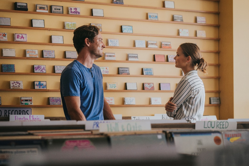 Laura (Clara Rugaard) und Harrison (Lewis Pullman) vor der Wand mit den vergessenen Mixtapes.
