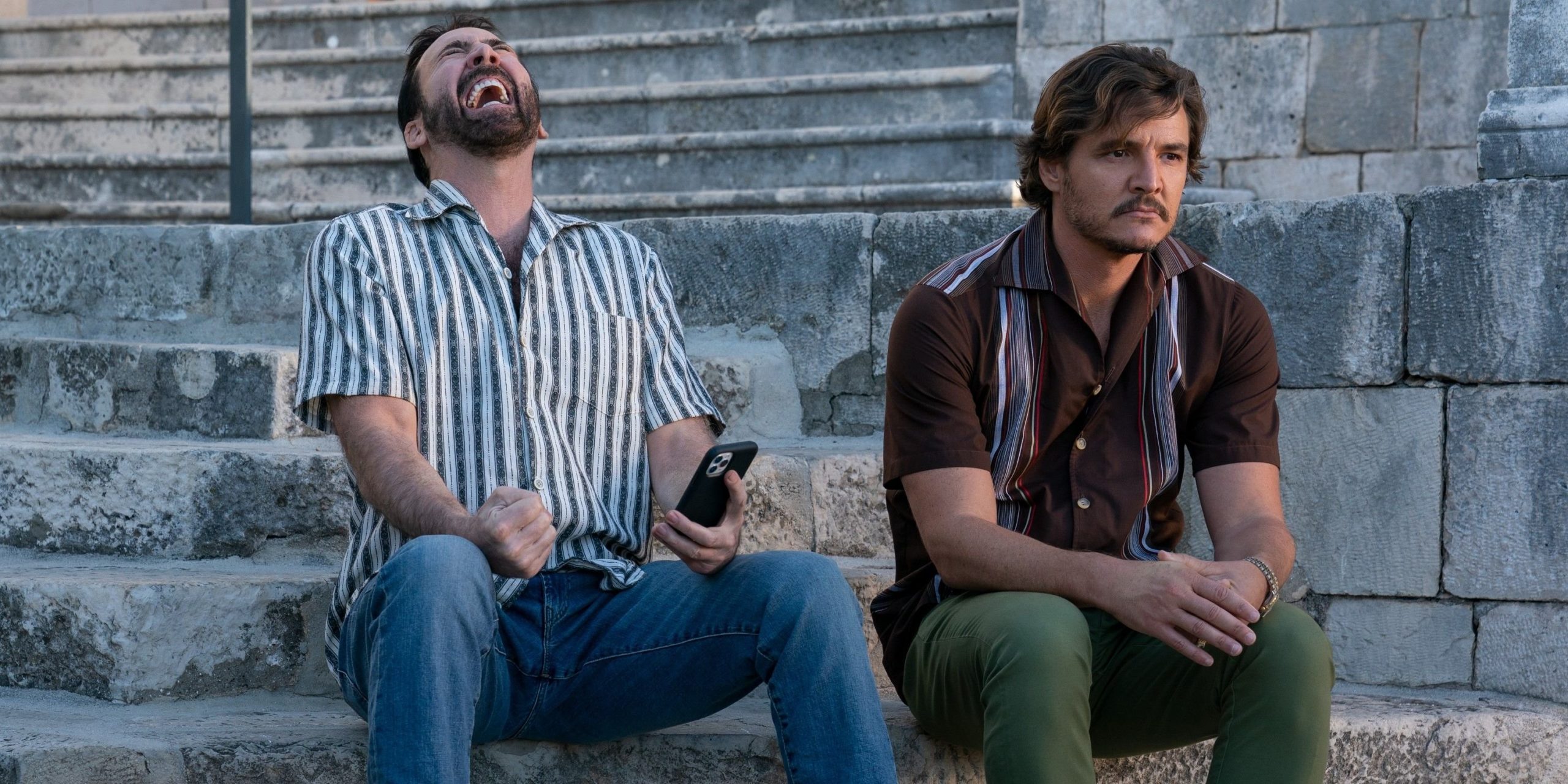 (l-R) Nicolas Cage und Pedro Pascal sitzen auf einer Steintreppe